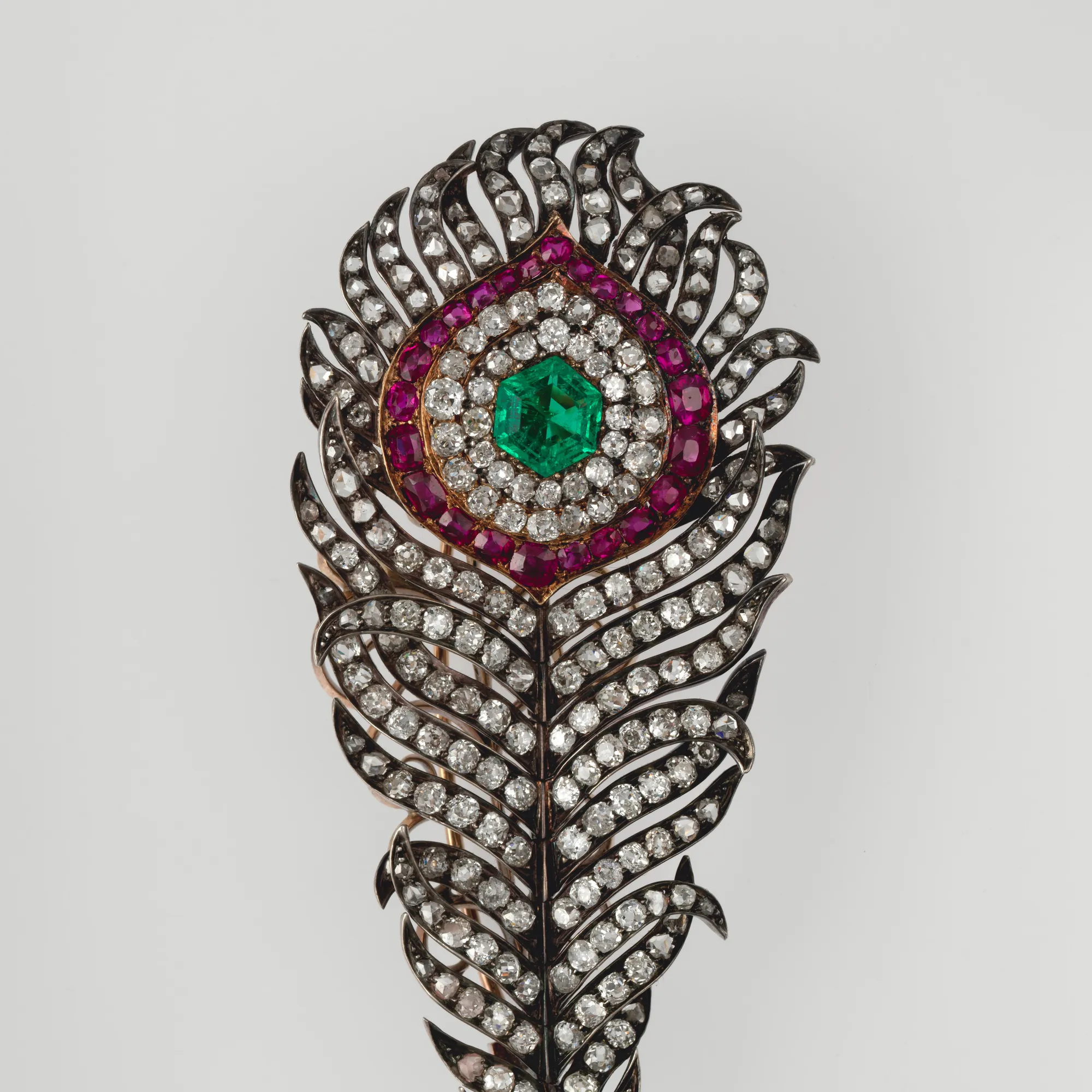 Detalle de un broche de pluma de pavo real: esmeralda central rodeada de rubíes y diamantes